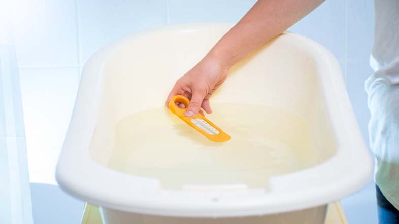 a parent measuring the temperature of the water in a plastic bath tub for their baby's first bath